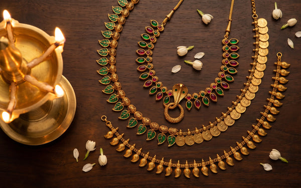 Flat-lay of traditional Kerala gold jewellery including Palakka Mala, Nagapadam, Kasu Mala and Manga Mala with jasmine and brass oil lamp
