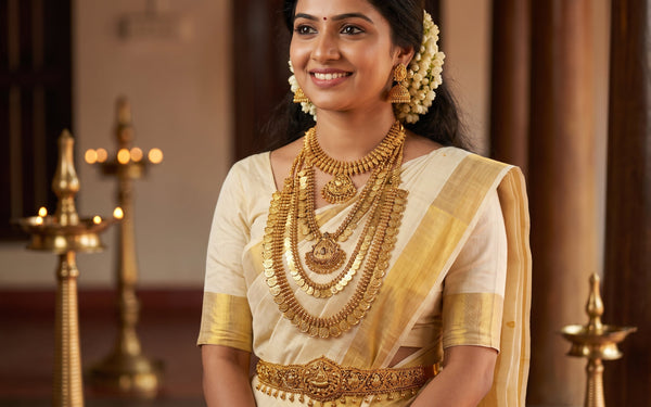 Kerala bride in cream kasavu saree wearing layered traditional gold bridal jewellery with Palakka Mala, Jhimki earrings and jasmine in hair