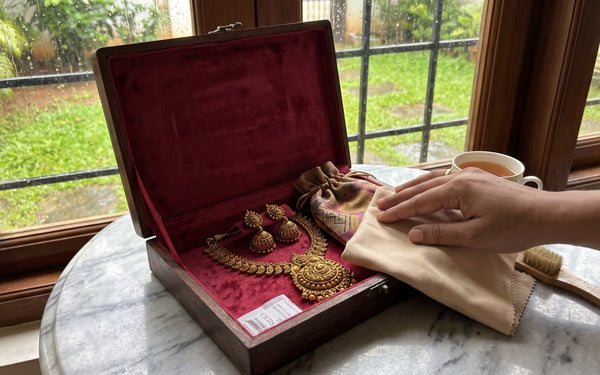 Antique gold South Indian temple necklace and jhumkas stored in a lined wooden jewellery box with microfibre cloth on a marble surface