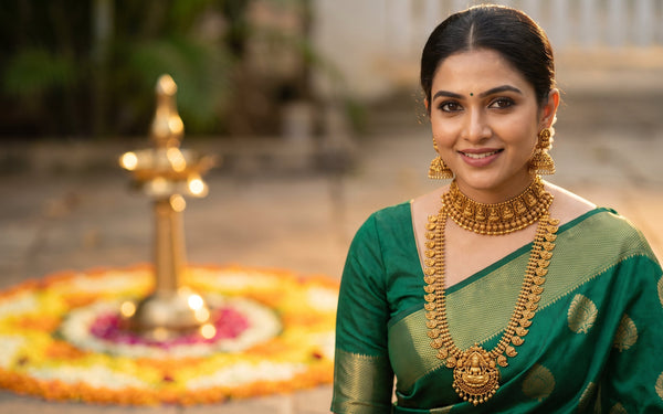 Modern South Indian woman wearing layered antique gold temple jewellery with Lakshmi haram and Jhimka earrings over an emerald green silk saree